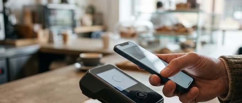 Смартфон у терминала бесконтактной оплаты в кафе